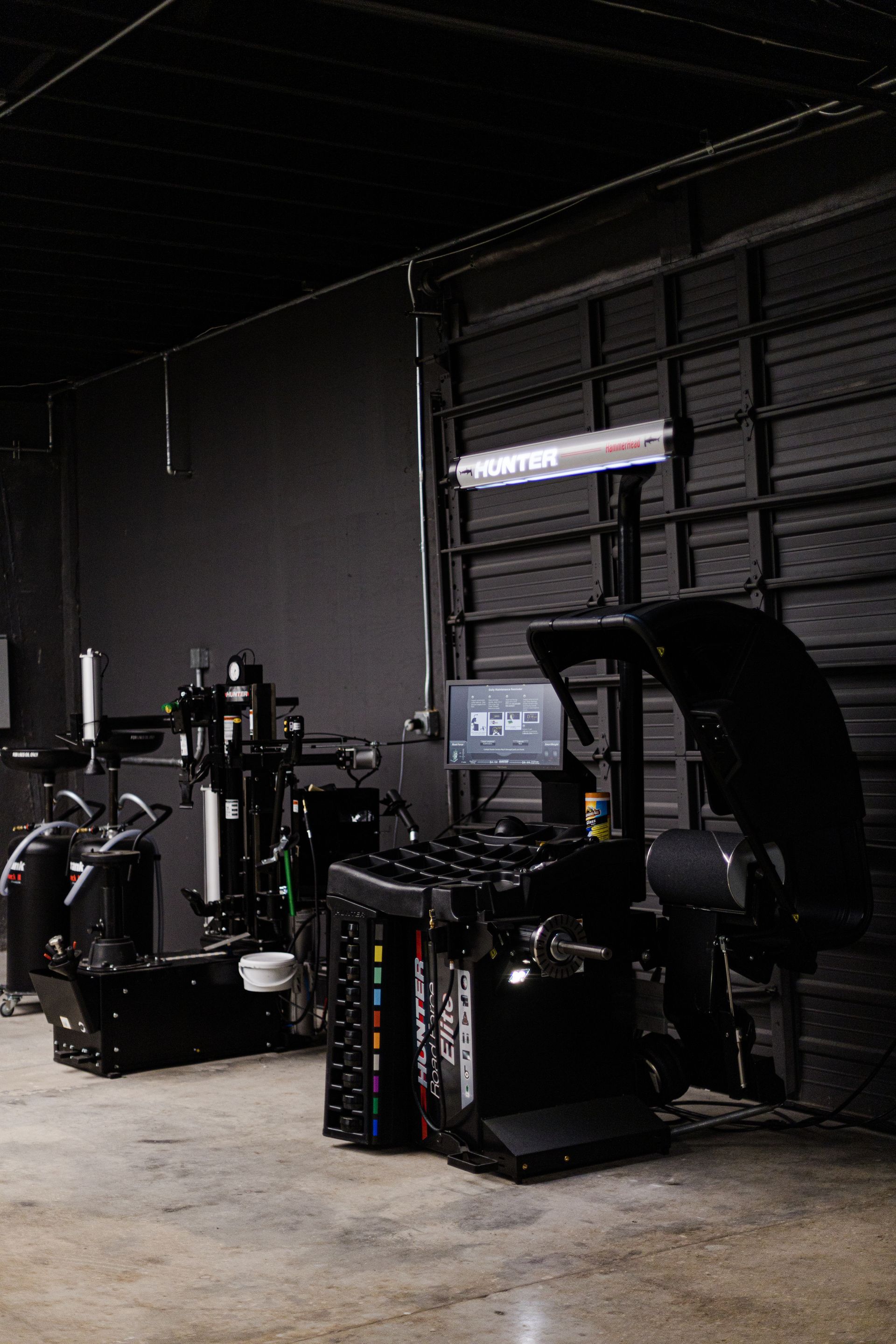 Two industrial tire service machines in a dark garage with concrete floors.