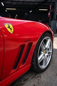 Red Ferrari sports car close-up, showing front wheel and side vents in a garage