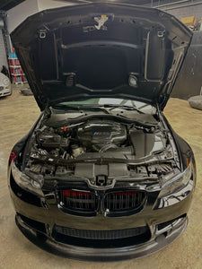 BMW sedan with hood open, exposing the engine bay in a workshop.