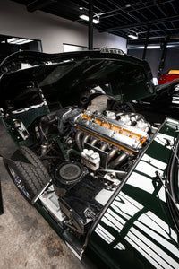 Classic black car with open hood, showing a polished engine in a garage or showroom.
