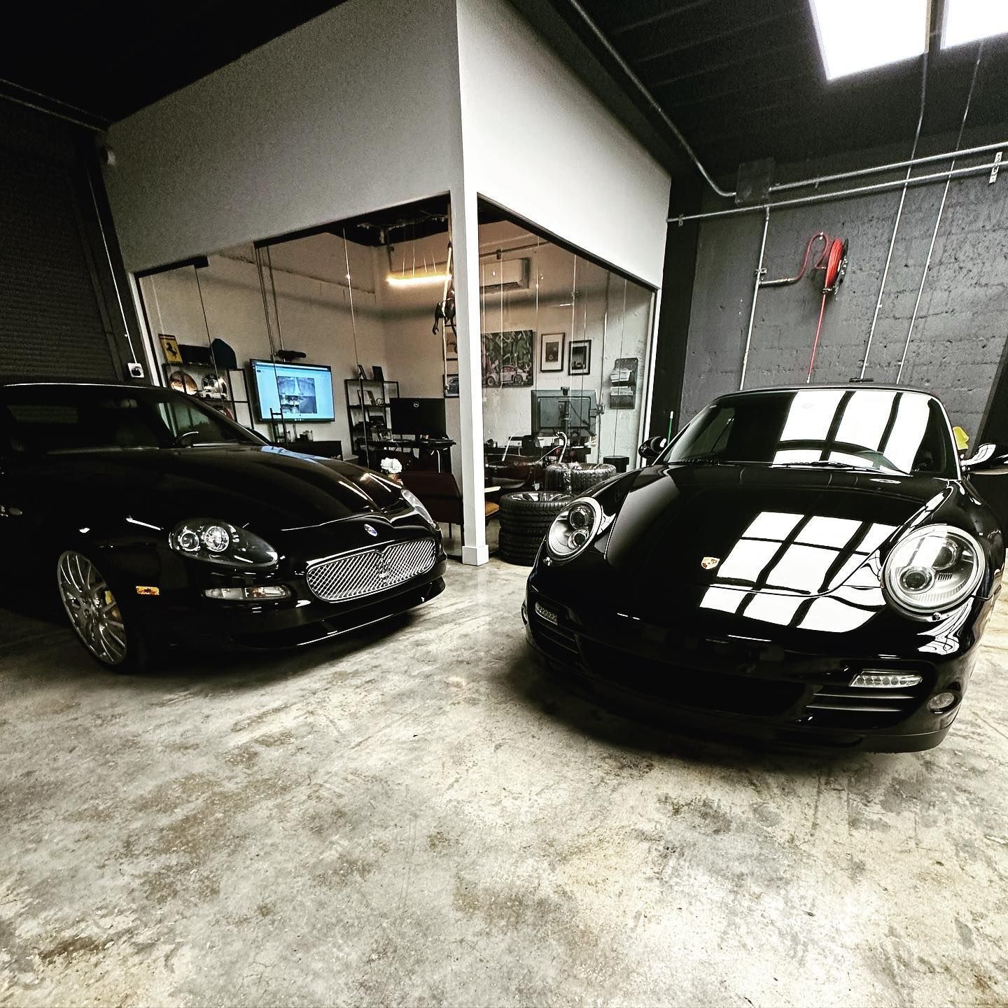 Two black cars, a Jaguar and a Porsche, parked inside a garage.
