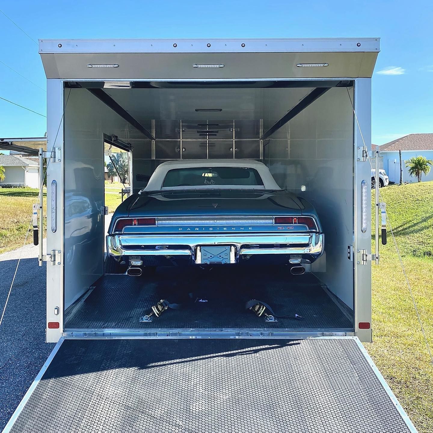Dark green convertible car inside an open silver trailer, on a sunny day.