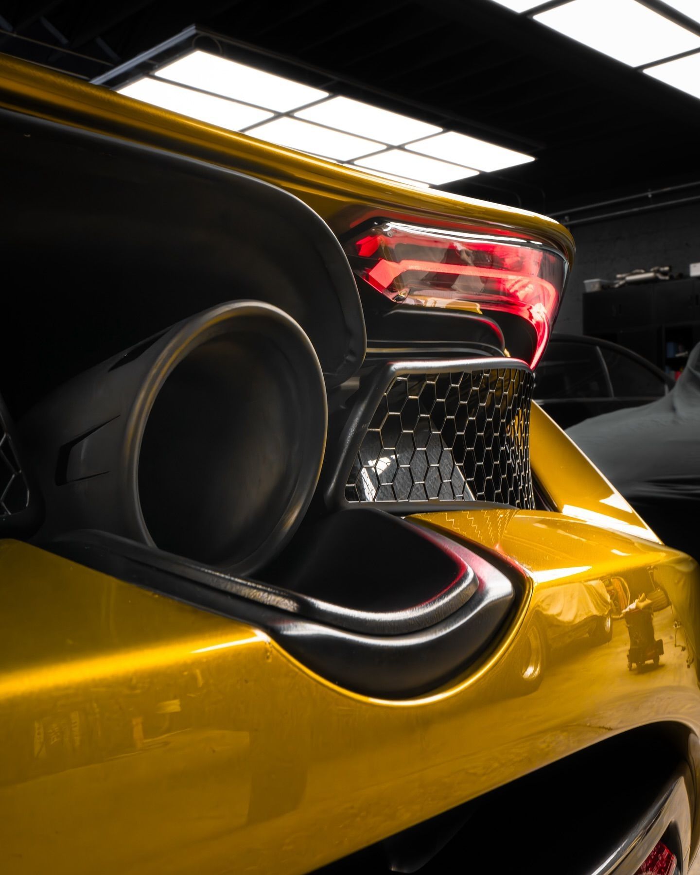 Close-up of a yellow sports car's exhaust pipe, taillight, and rear panel in a garage.