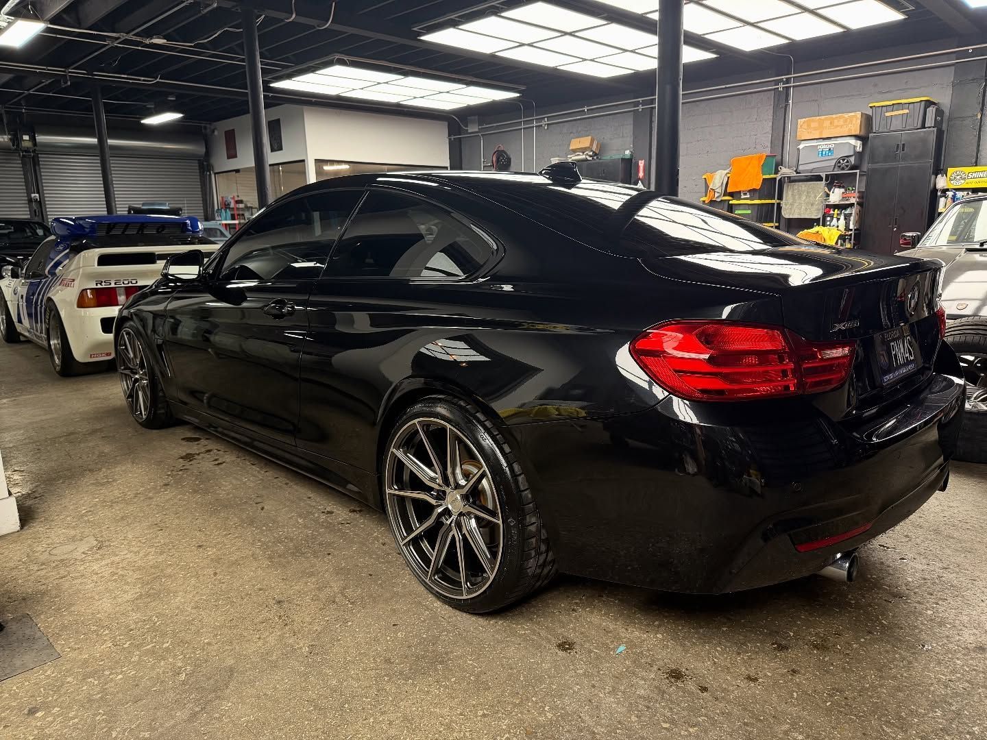 Black BMW coupe with tinted windows parked inside a garage, with a white car visible to the left.