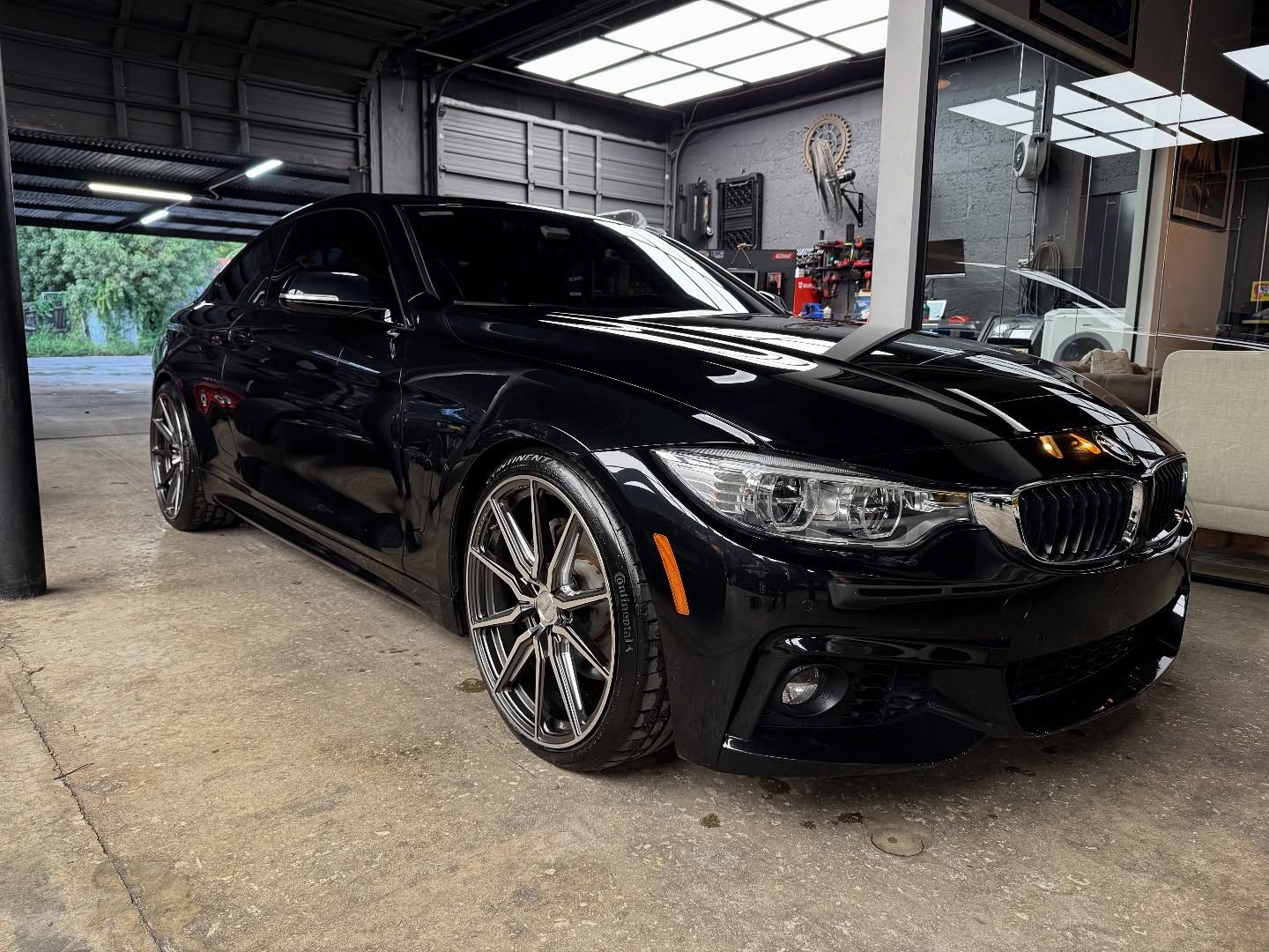 Black BMW coupe in a garage, shiny wheels, front view.