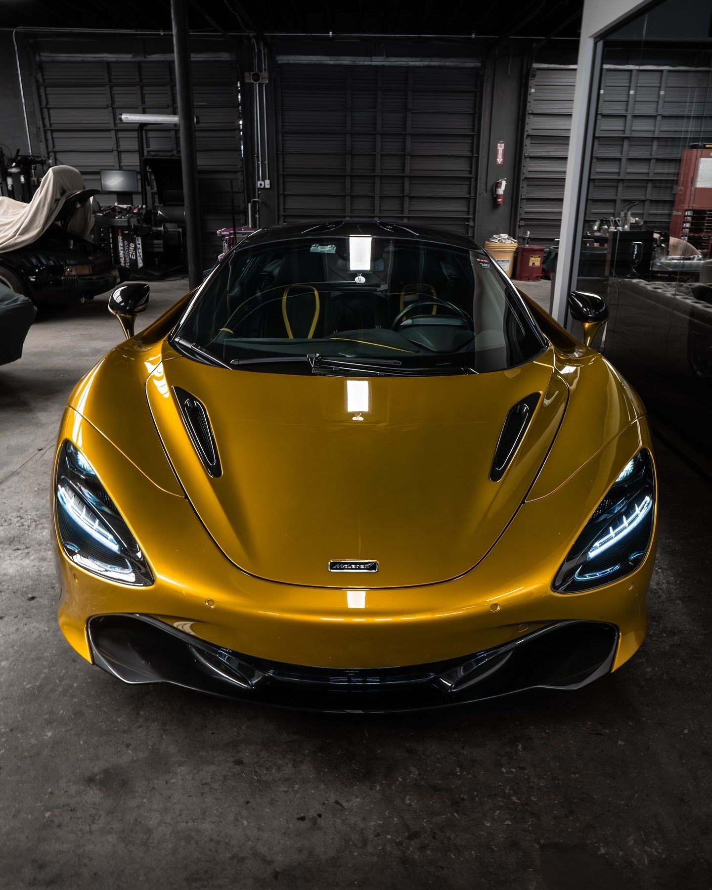 Golden McLaren sports car in a garage, facing the camera.
