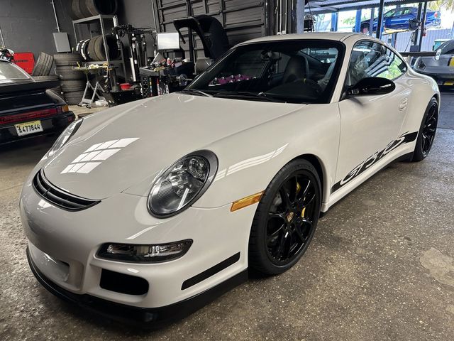 White Porsche sports car in a garage, with black wheels and hood graphics.
