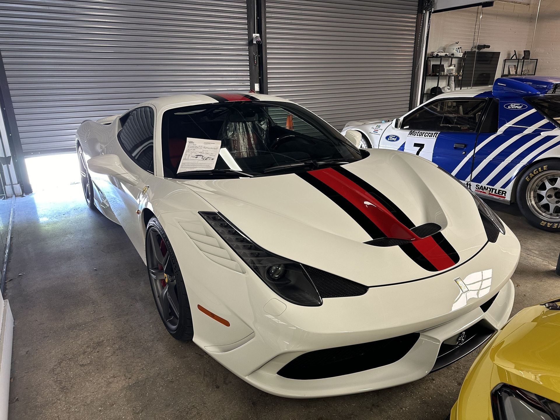 White Ferrari with red stripe, parked inside garage, another race car in background.