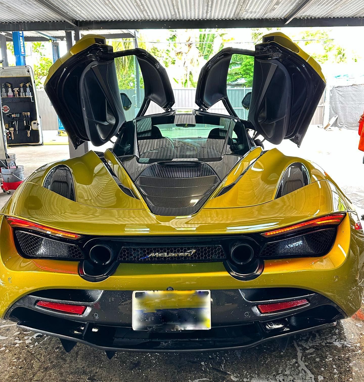 Yellow McLaren sports car with butterfly doors open. Rear view, parked in a car wash bay.