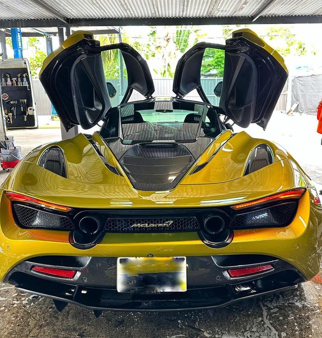 Yellow McLaren sports car, doors open upward, parked in a car wash.