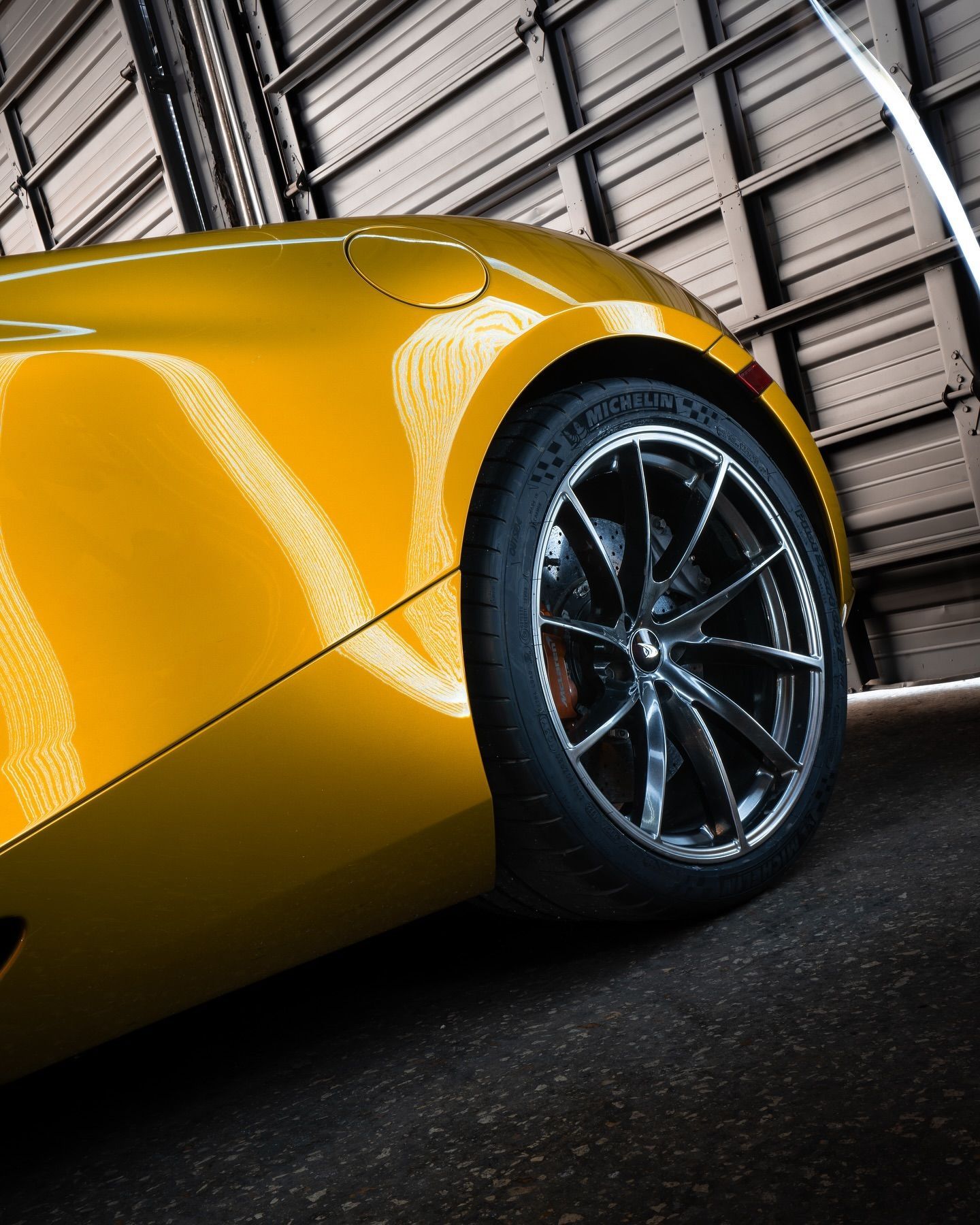 Yellow sports car with black wheel and tire, inside a garage.