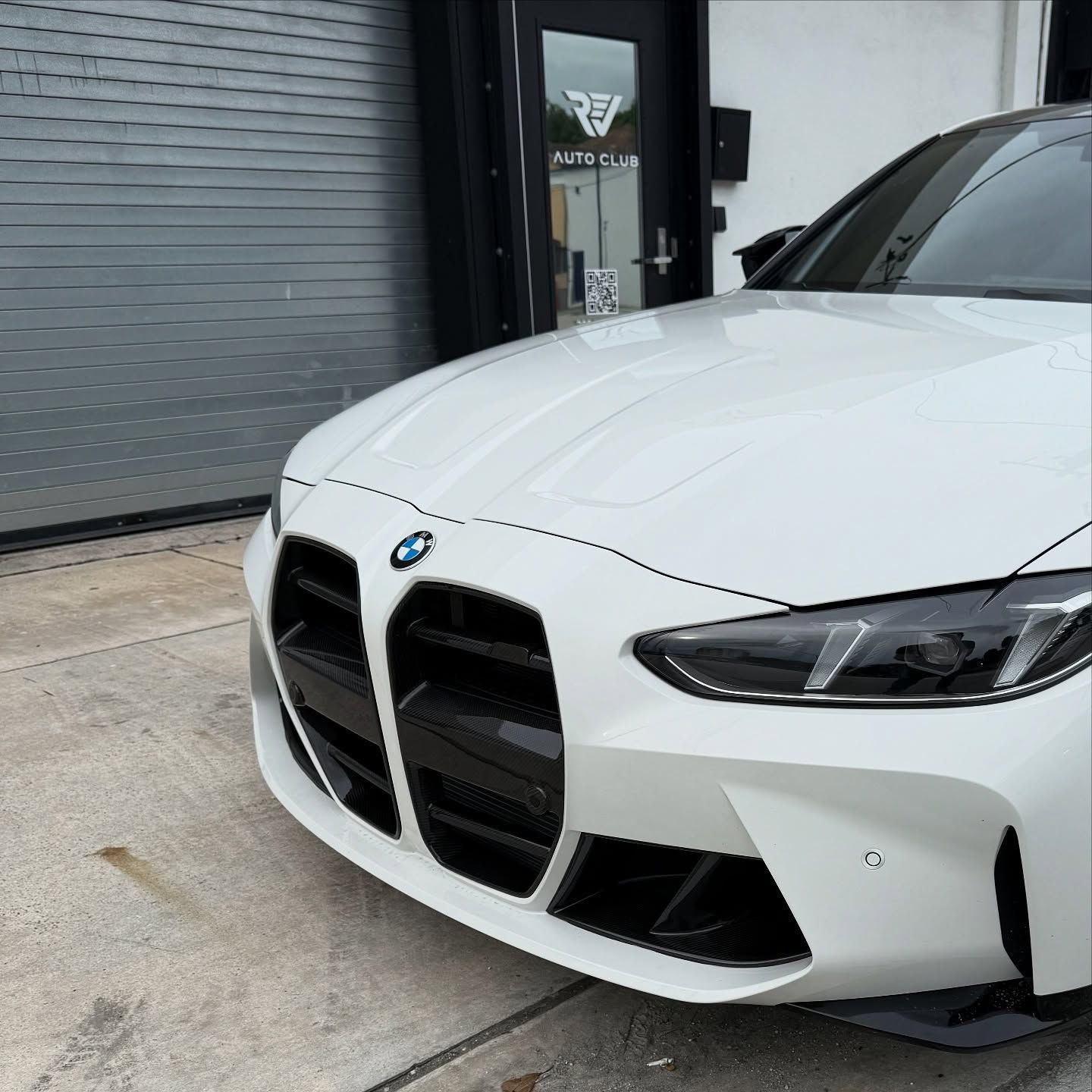 White BMW M4 sports car parked outside a building with a black door and garage door.
