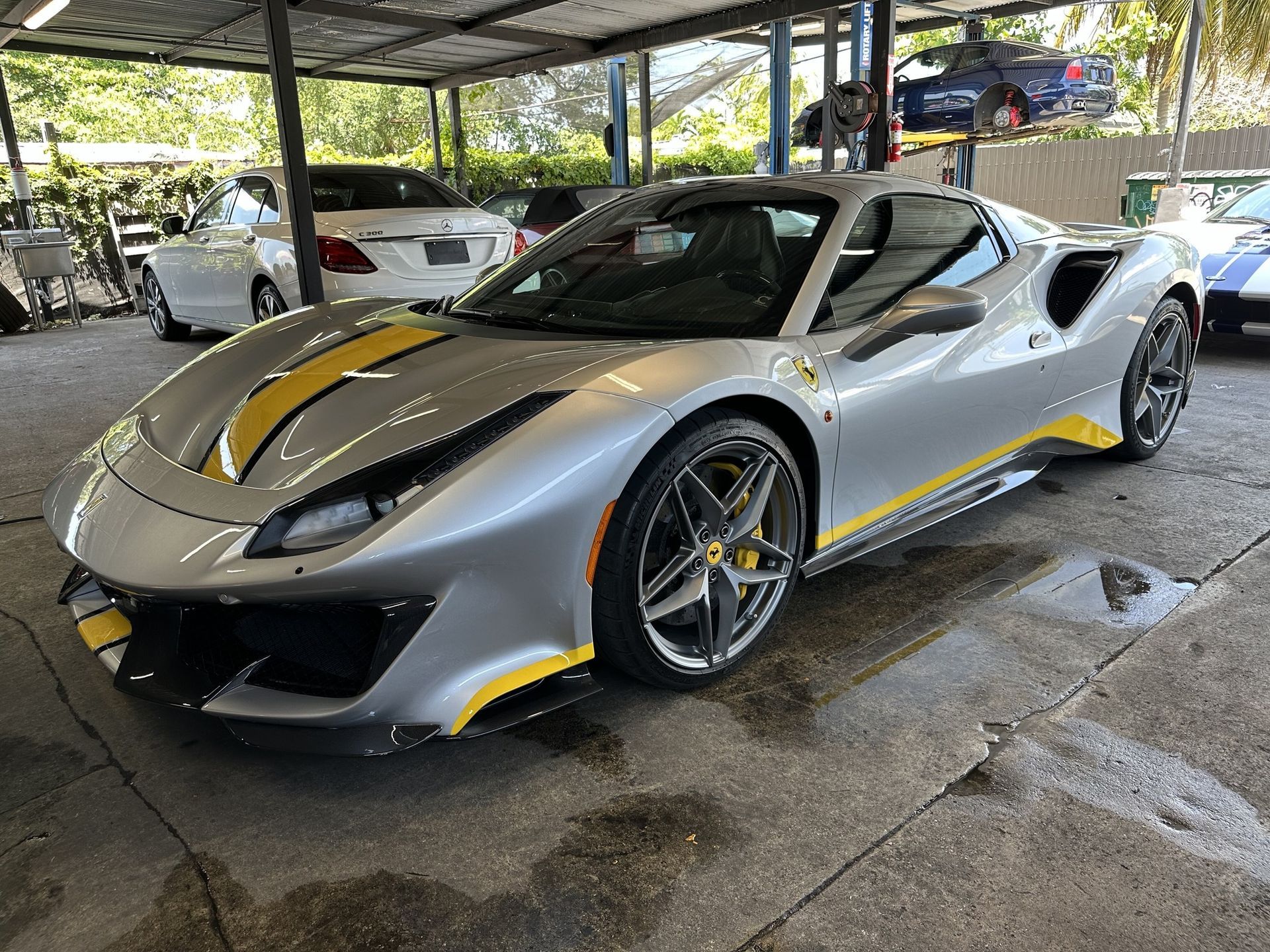 Silver Ferrari with yellow racing stripes parked under a metal awning.