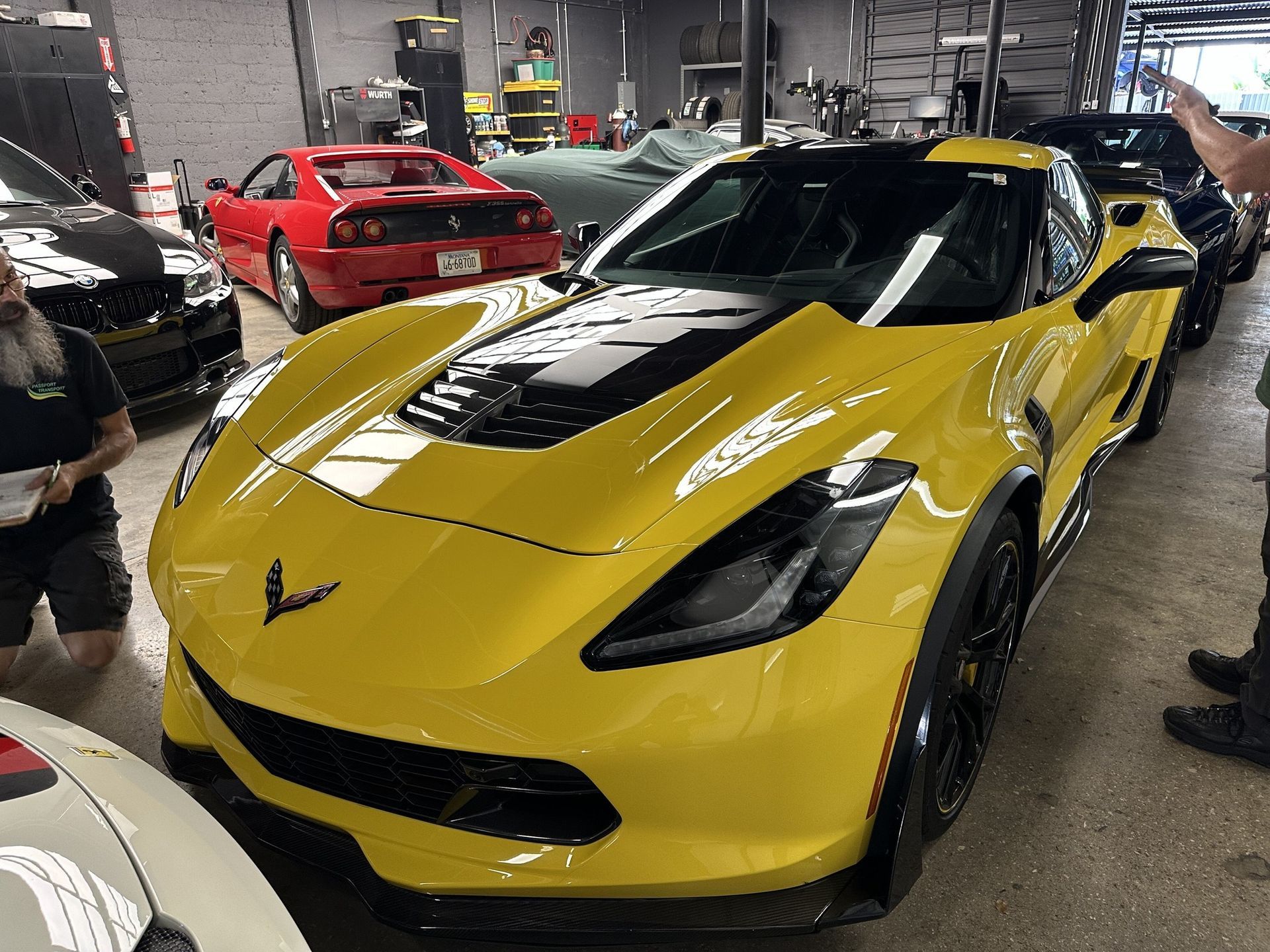 Yellow Corvette Z06 in a garage with a red Ferrari and other vehicles.