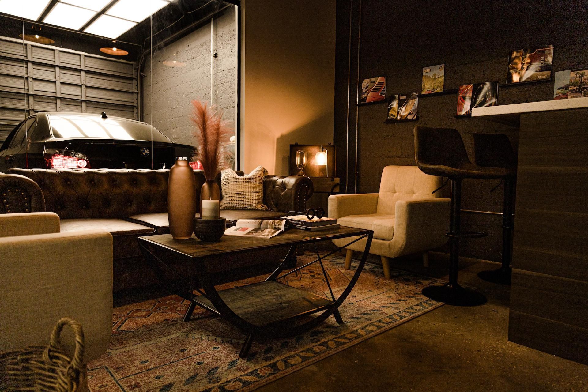 Cozy lounge with car visible through glass. Brown tones, seating, coffee table, and bar stools.