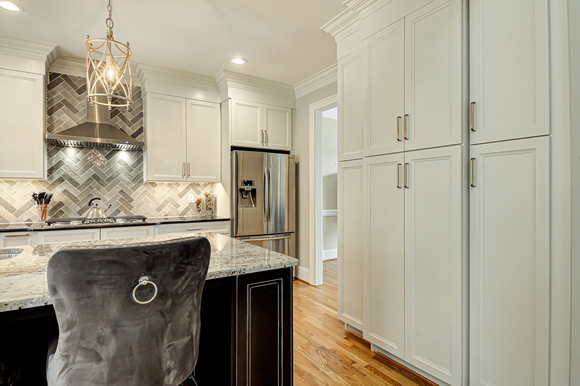 A kitchen with white cabinets, granite counter tops, stainless steel appliances, and a gray chair.