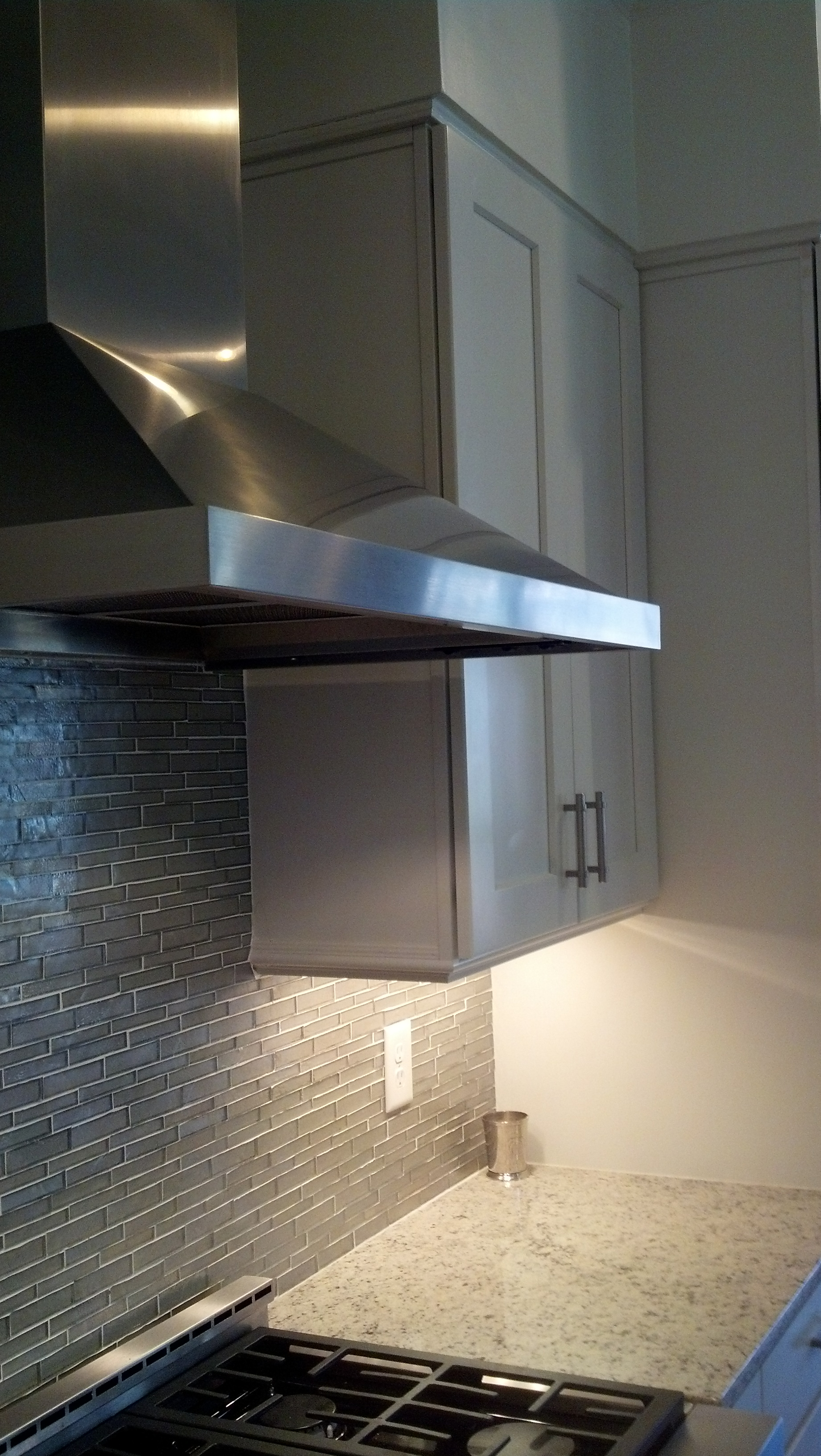 A stainless steel hood is hanging over a stove in a kitchen.
