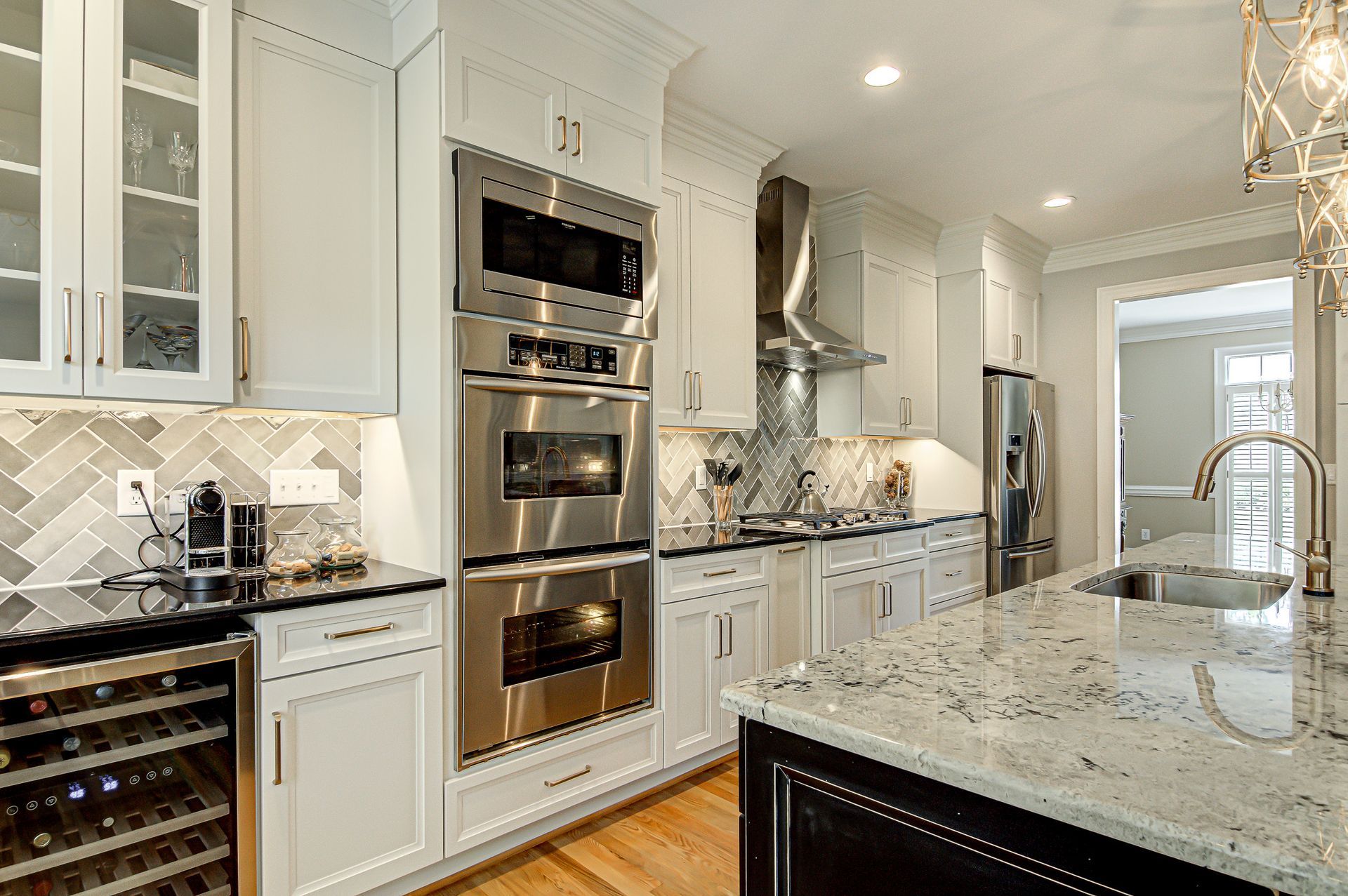 A kitchen with white cabinets, stainless steel appliances, granite counter tops, and a wine cooler.