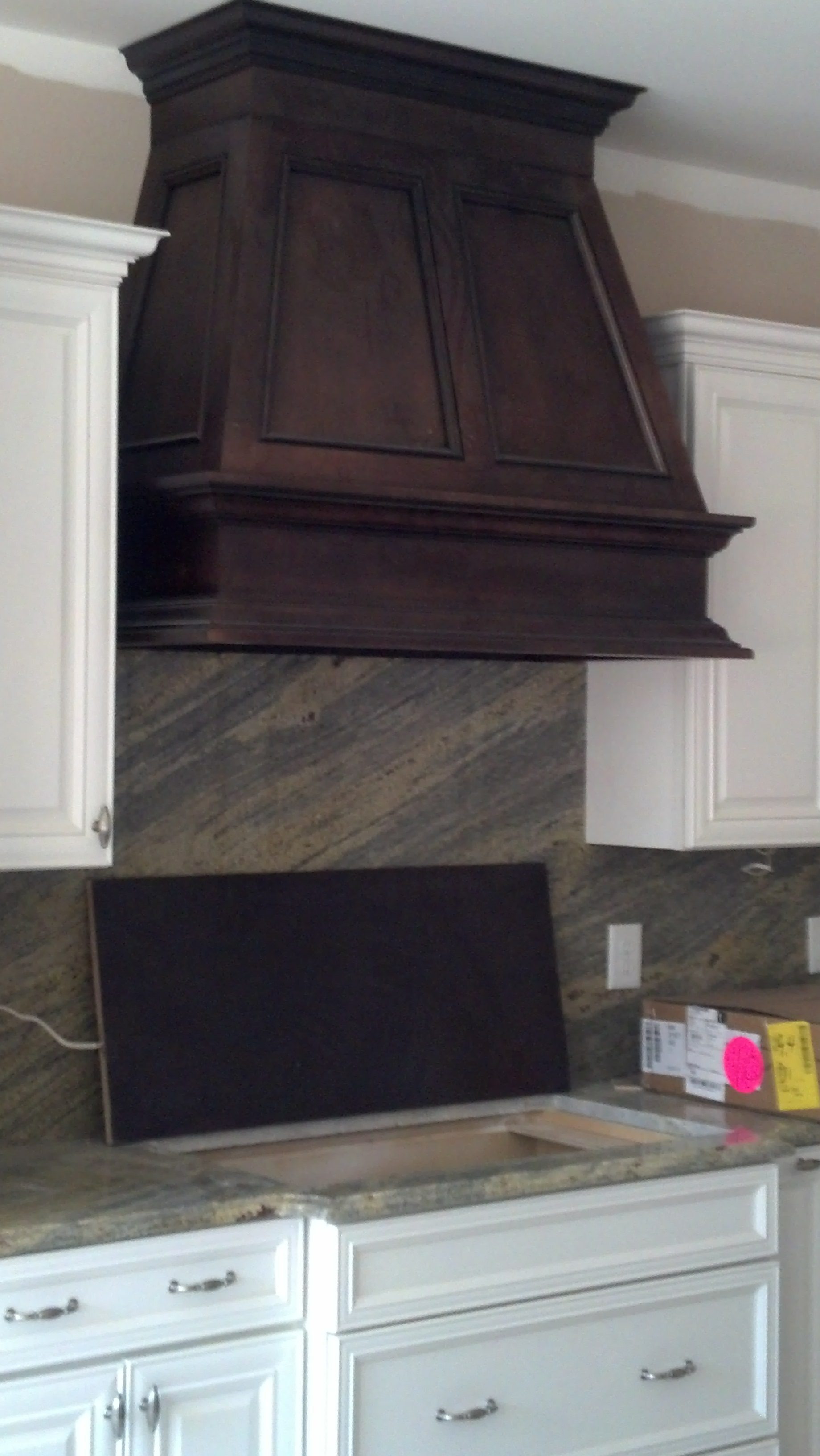 A kitchen with white cabinets and a wooden hood above the sink