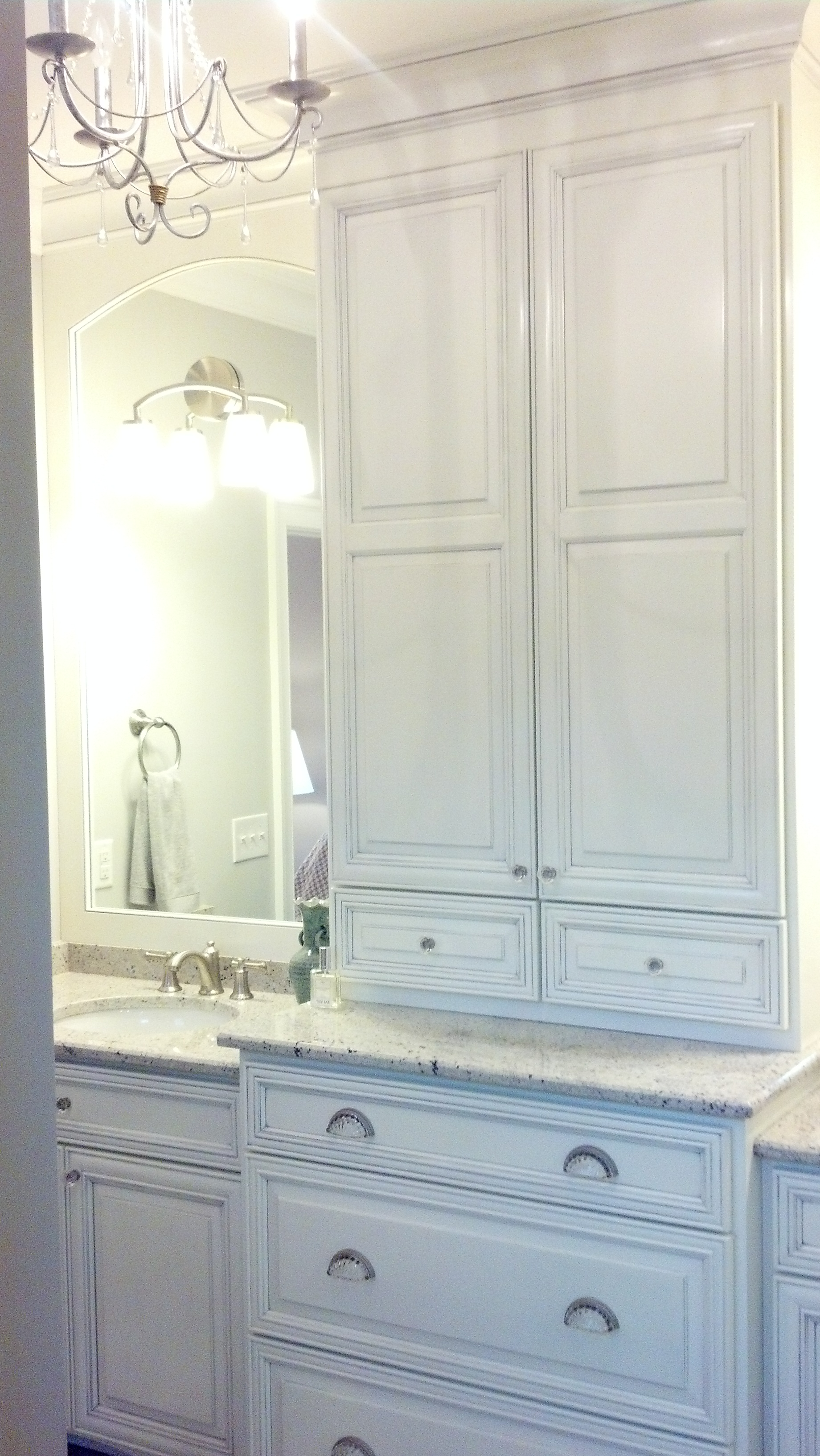 A bathroom with white cabinets , drawers , a sink and a mirror.