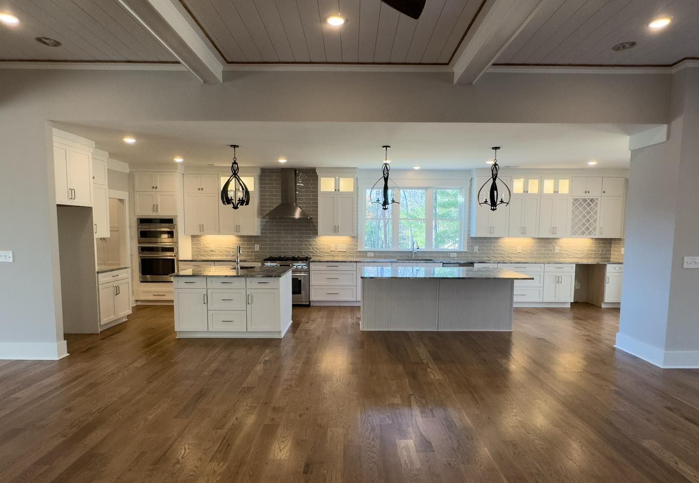 A large empty kitchen with white cabinets and hardwood floors.