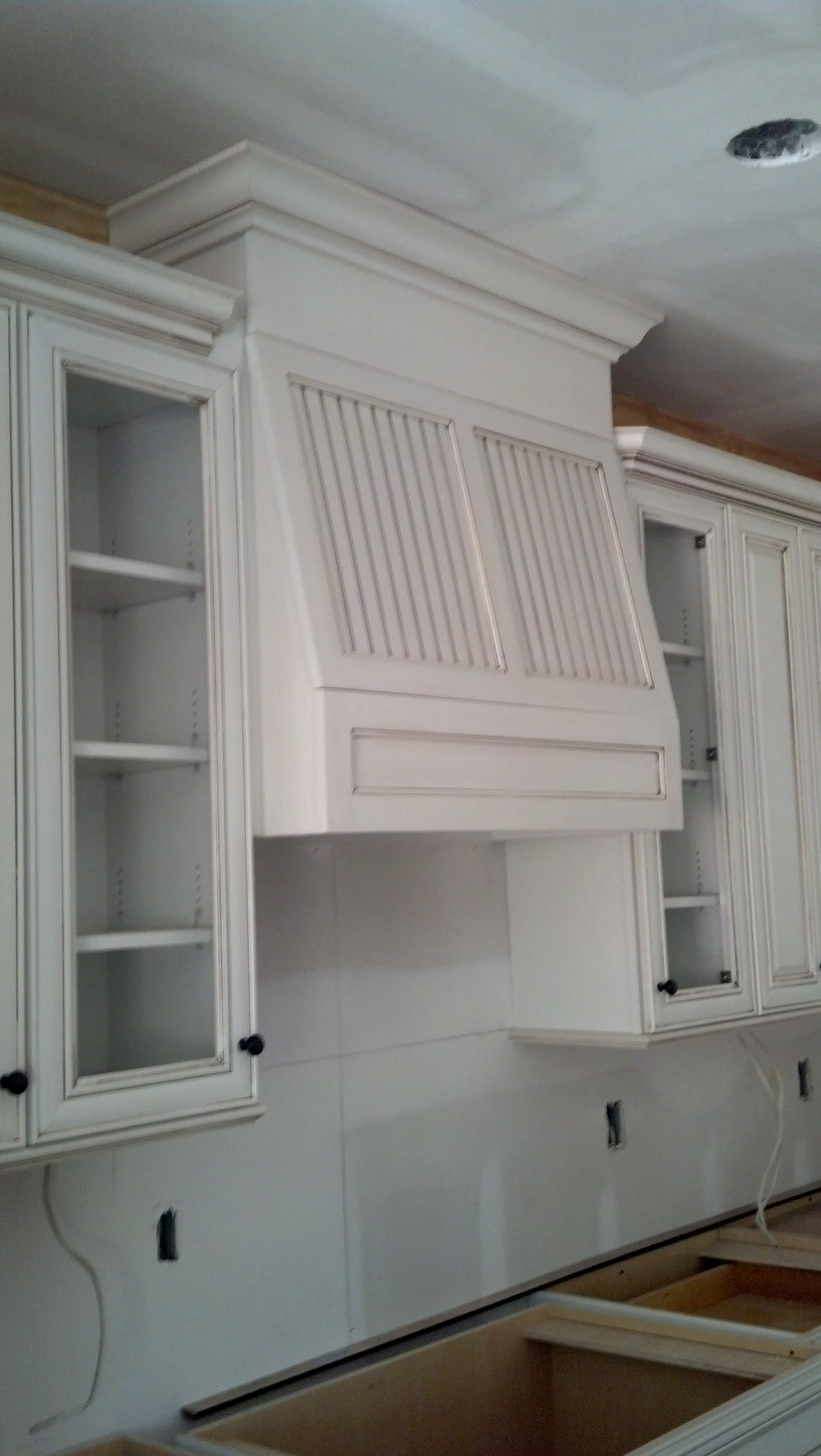 A kitchen with white cabinets and a hood above the sink.