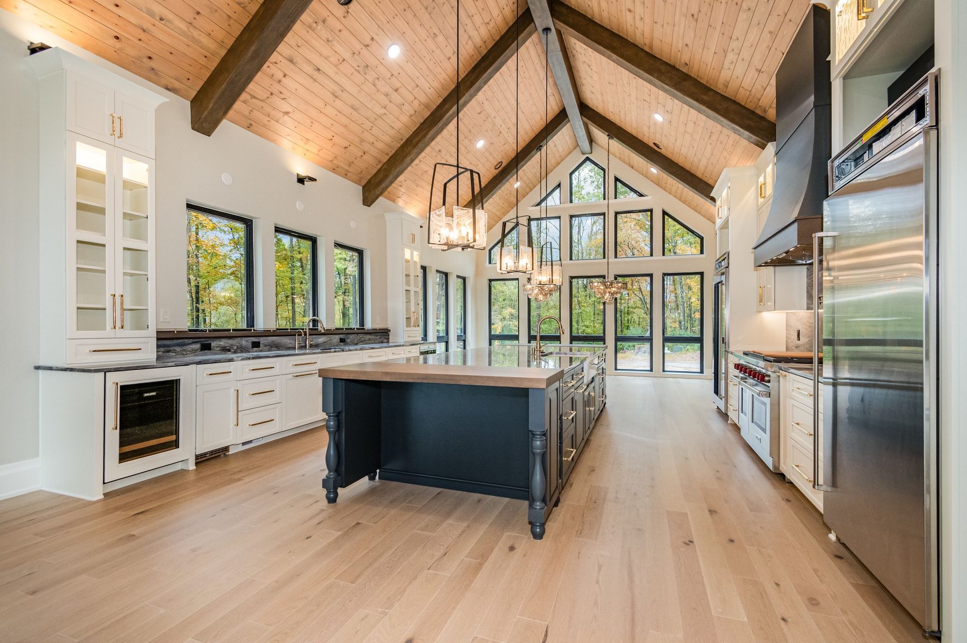 Spacious kitchen with wood ceiling, island, white cabinets, and stainless steel appliances. Large windows with an outdoor view.