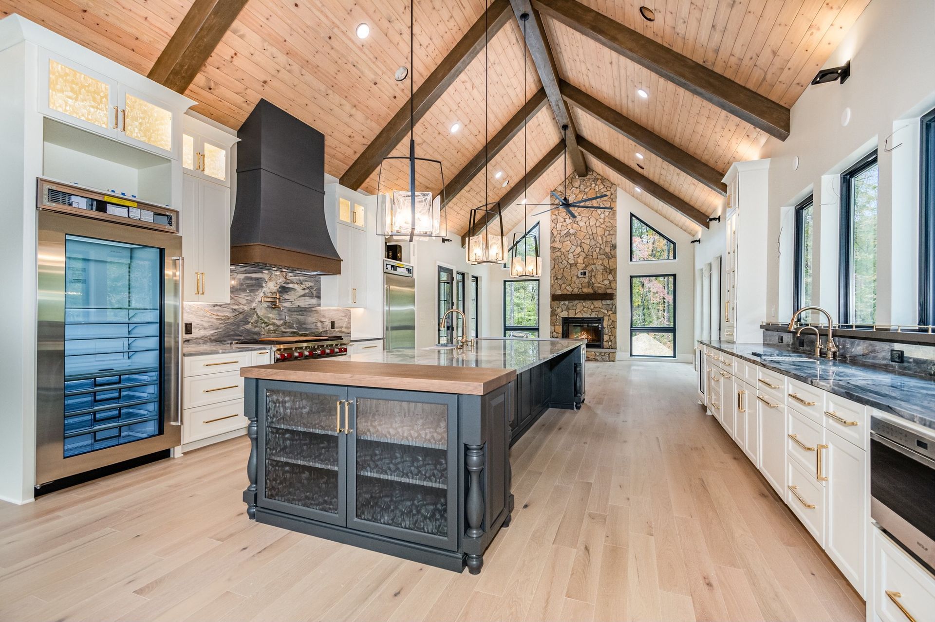 Spacious kitchen with wood ceiling, island, and large wine fridge. Fireplace in the background.