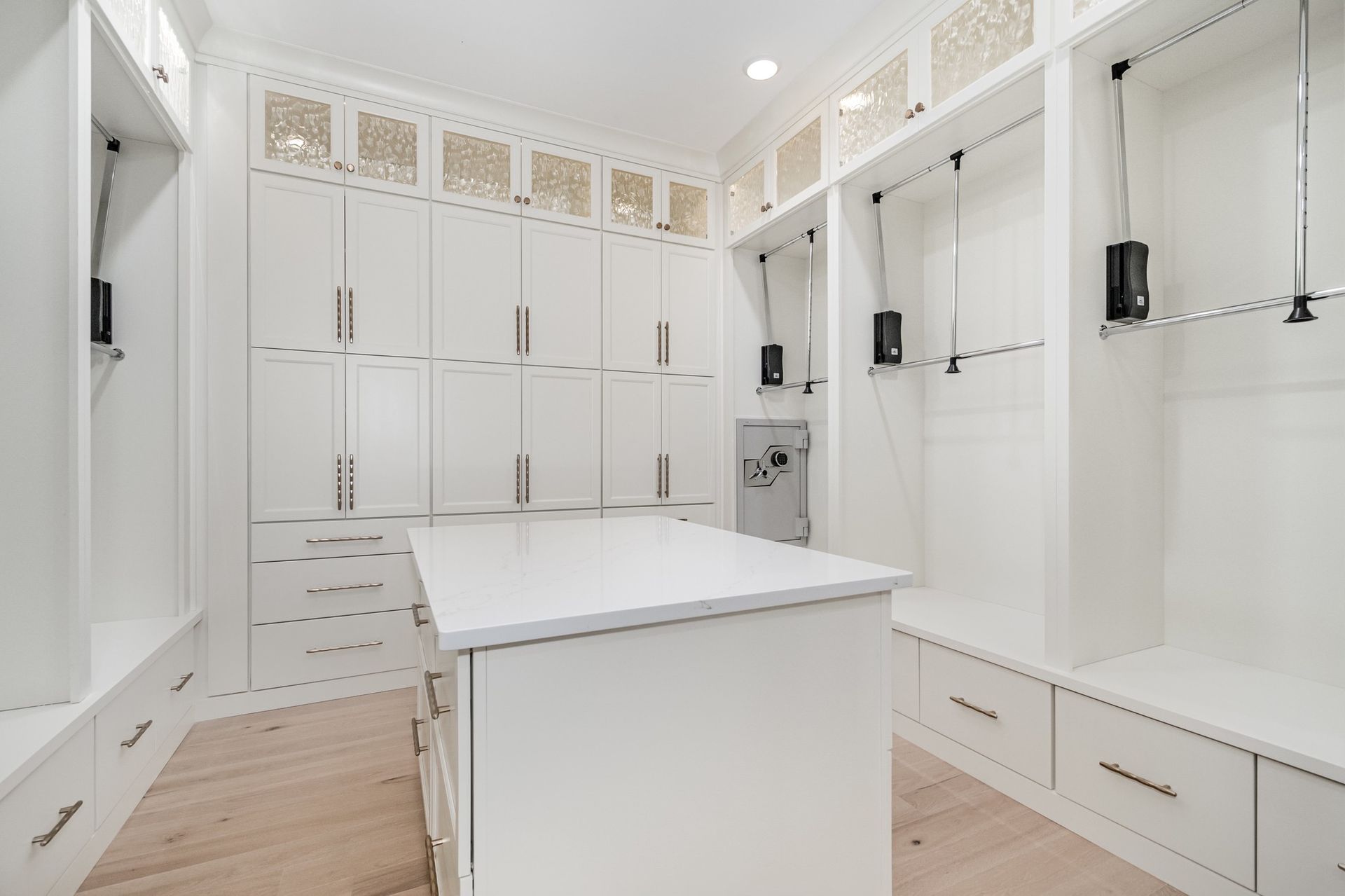 White walk-in closet with island, cabinets, hanging rods, and drawers; light wood floors.