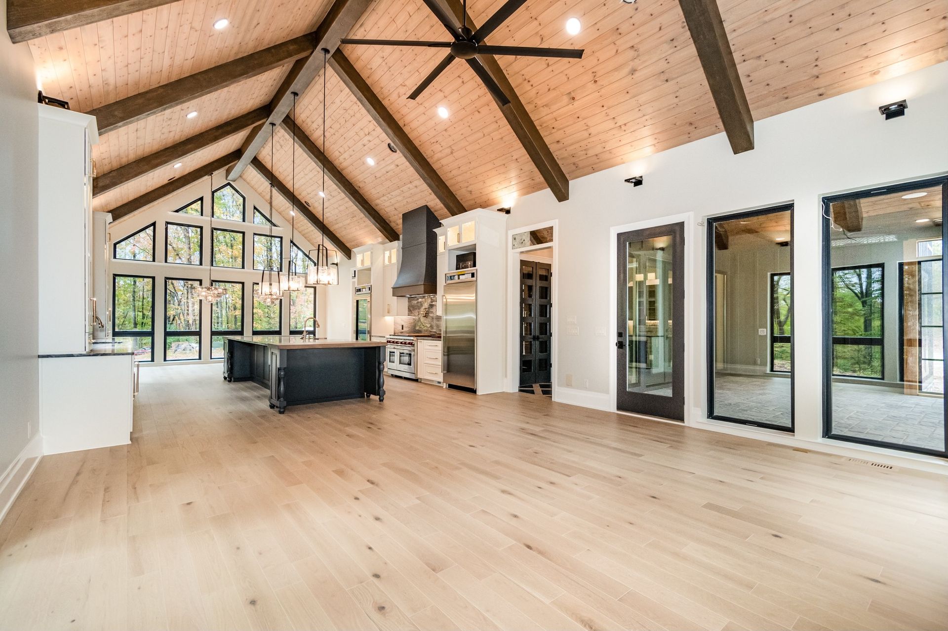 Spacious interior with vaulted wood ceiling, light wood floors, and black kitchen island.