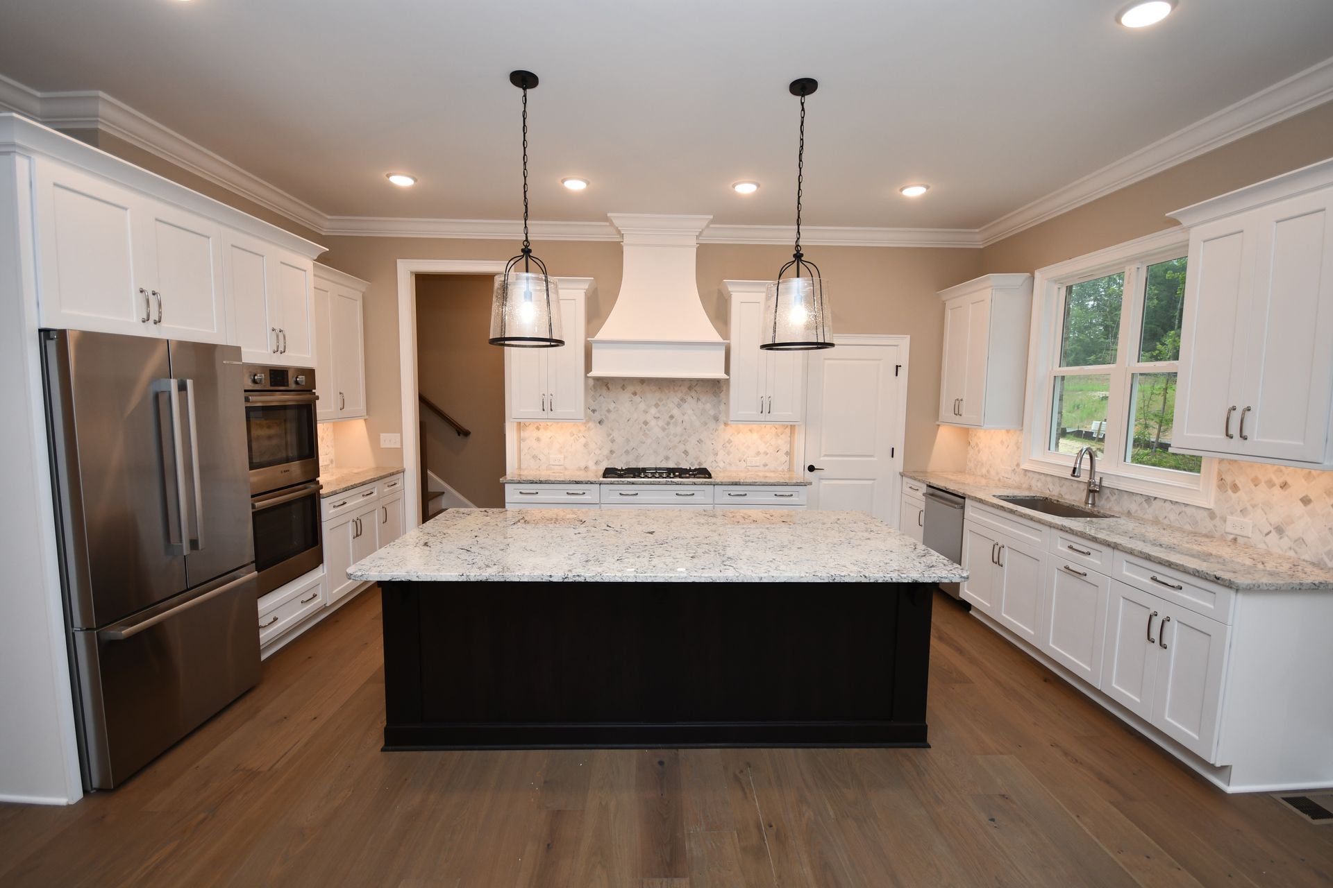 A kitchen with white cabinets , granite counter tops , stainless steel appliances and a large island.