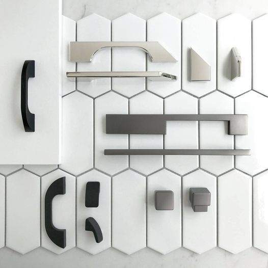 A variety of cabinet handles are displayed on a white tile wall