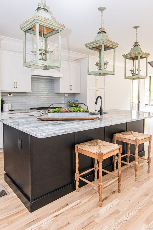 A kitchen with a large island , stools and lanterns hanging from the ceiling.