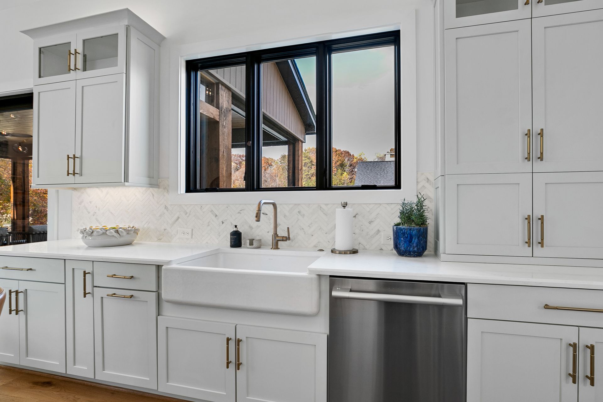 White kitchen with cabinets, sink, window, and stainless steel dishwasher.