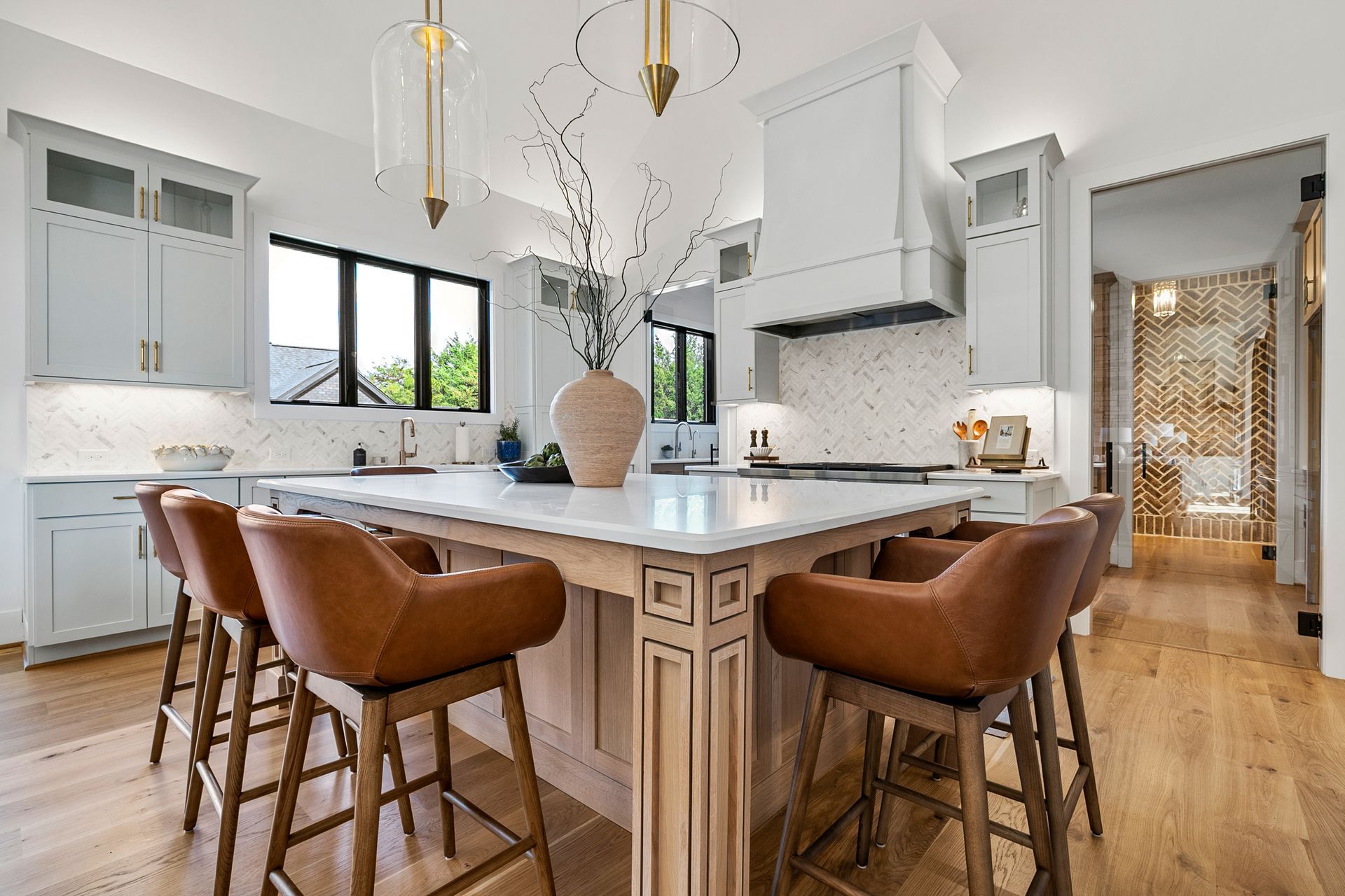 Modern kitchen with light blue cabinets, white countertops, and leather bar stools around a central island.