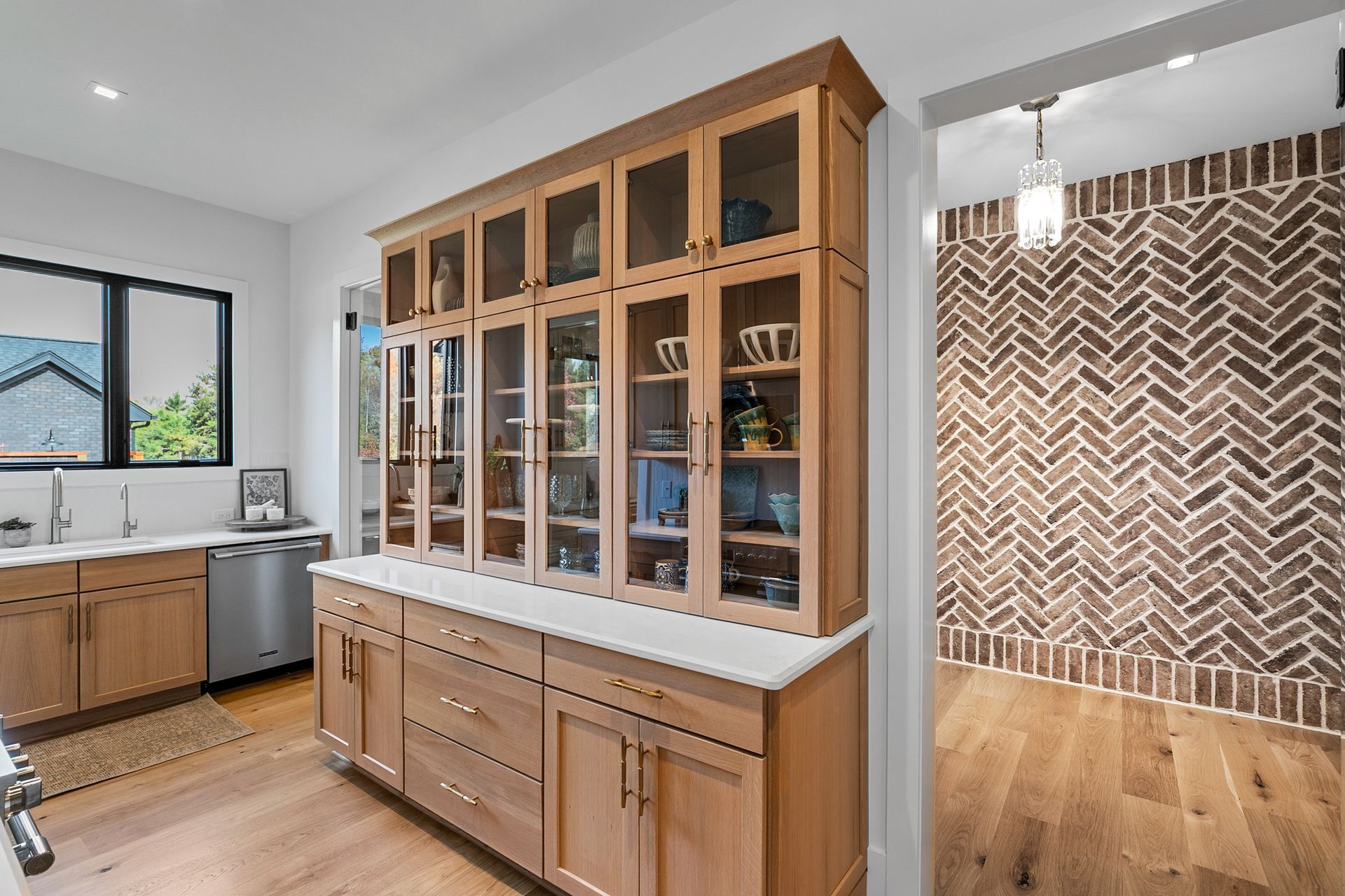 Wooden kitchen cabinet with glass doors, and a brick accent wall visible in the doorway.