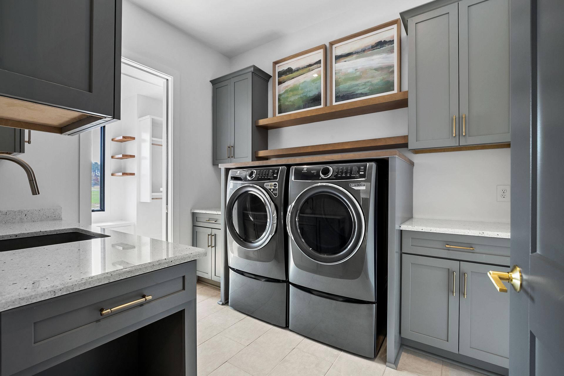 Modern laundry room with gray cabinets, washer/dryer, and artwork.