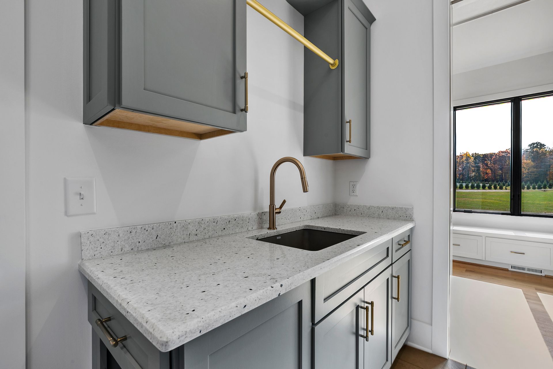 Gray cabinets and sink in a modern laundry room with white speckled countertop, gold hardware and rod.
