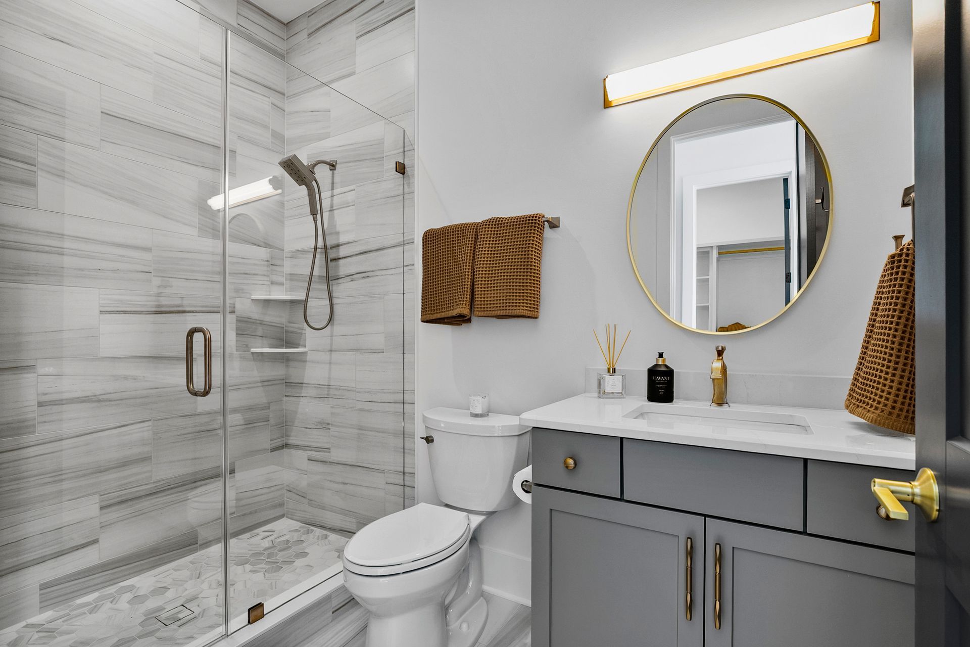 Modern bathroom with gray vanity, glass shower, marble tile, and gold accents.