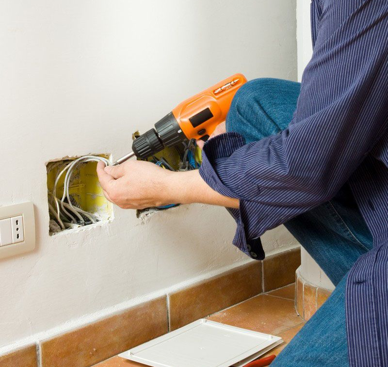 Electrician working on wiring in a wall, using a drill.