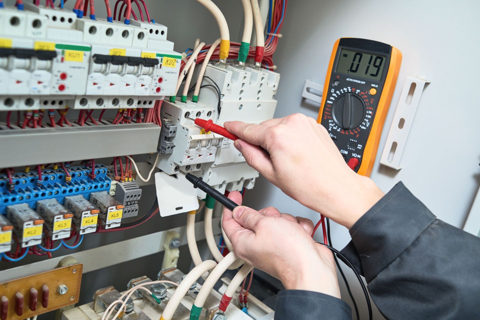 Electrician using a multimeter to test wiring in an electrical panel.