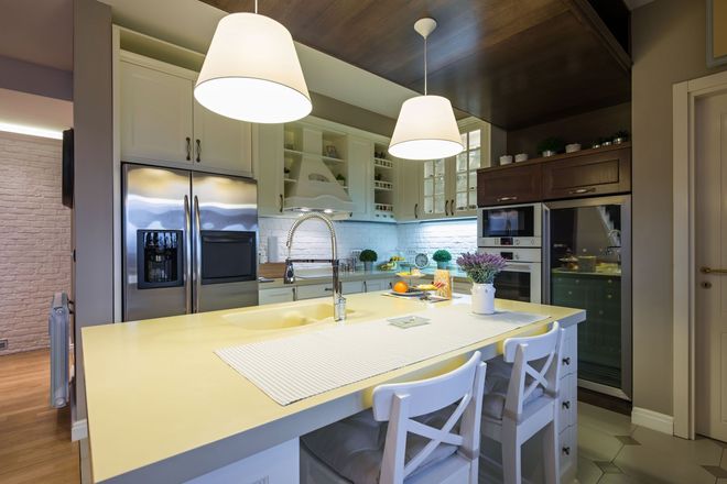 Modern kitchen with white island, hanging pendant lights, stools, and stainless steel appliances.