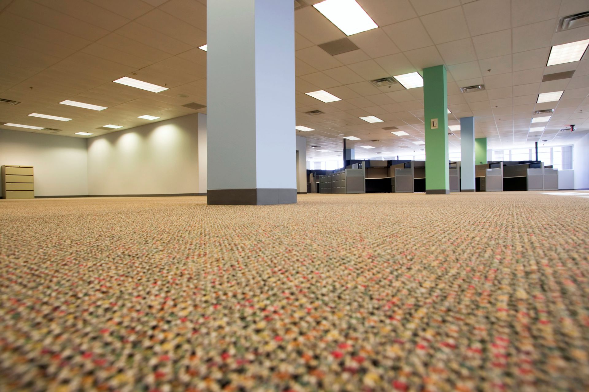 Empty office interior with carpeted floor, fluorescent lights, and support columns.