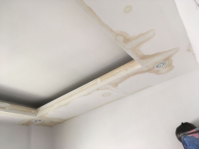 Damaged ceiling corner with water stains and peeling trim near a light fixture.
