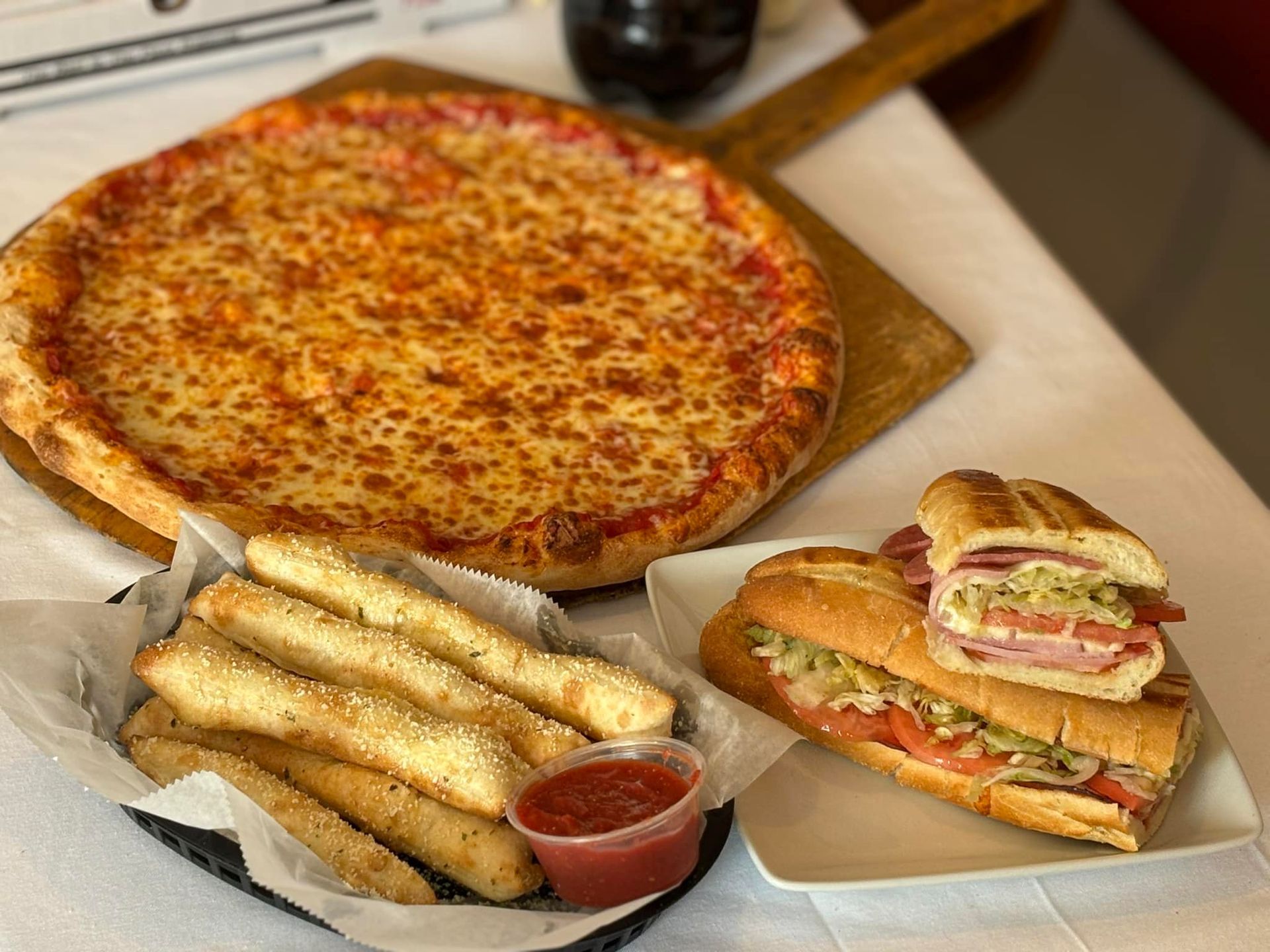 A pizza , mozzarella sticks , and a sub sandwich are on a table.
