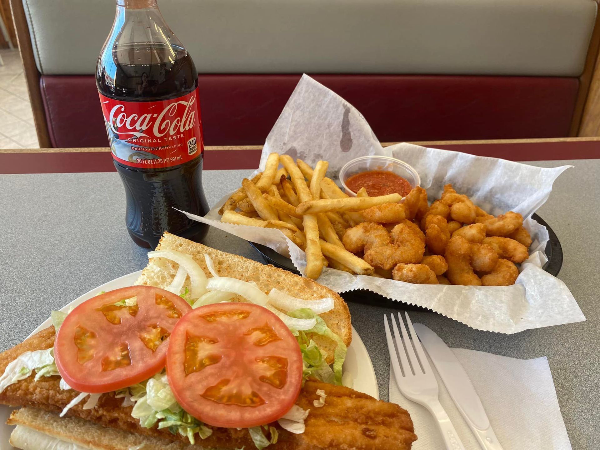 A sandwich , french fries and shrimp are on a table next to a bottle of coca cola.