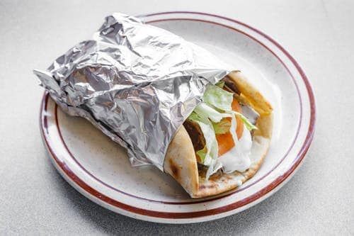 A gyro sandwich wrapped in tin foil on a plate.