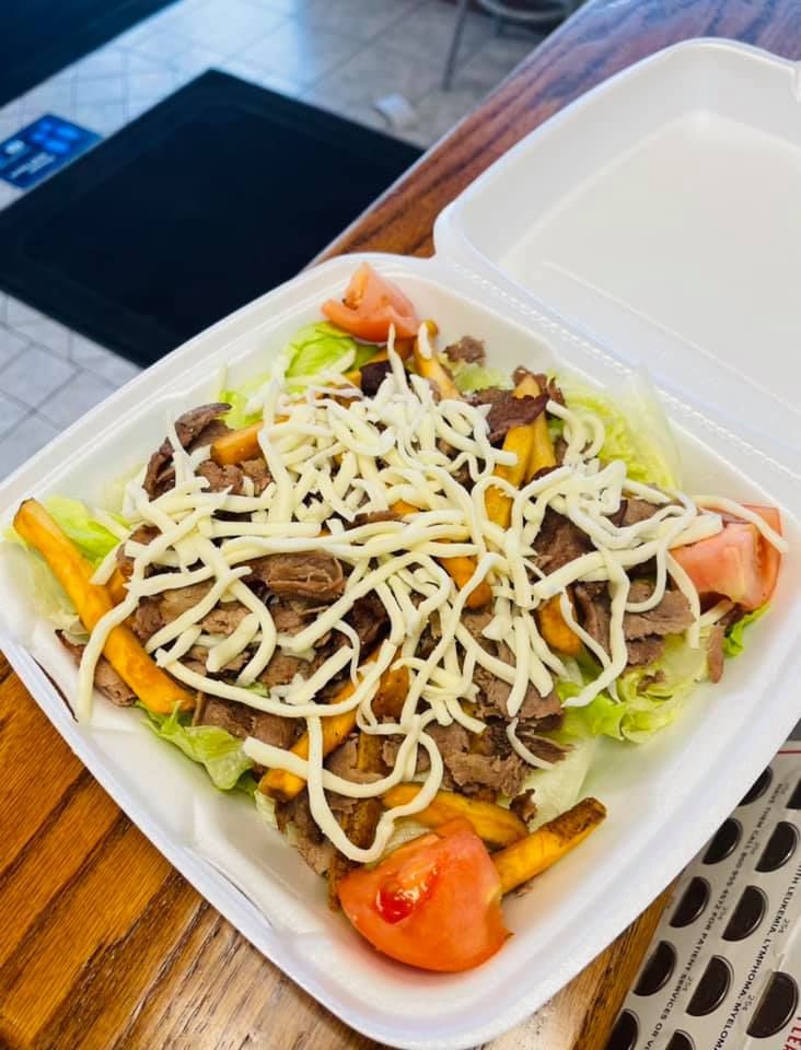 A styrofoam container filled with french fries , lettuce , tomatoes and cheese.