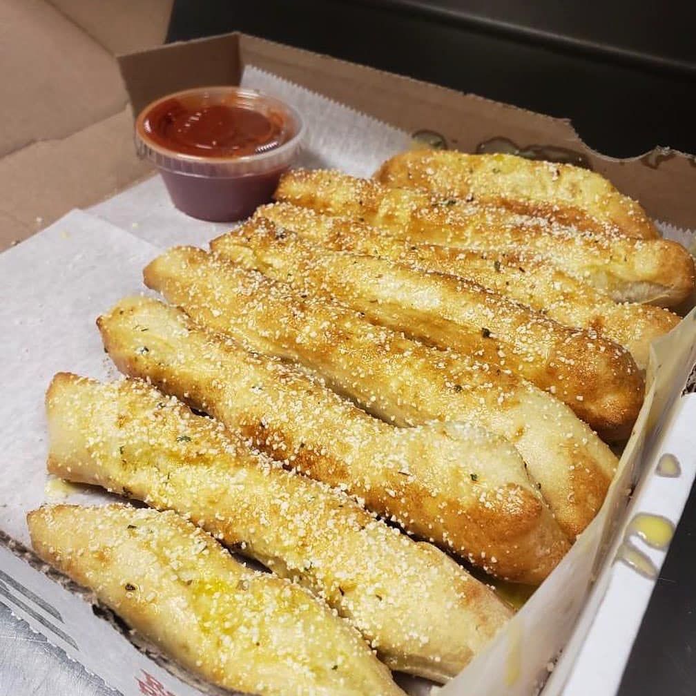 A box of garlic bread sticks with a side of ketchup.