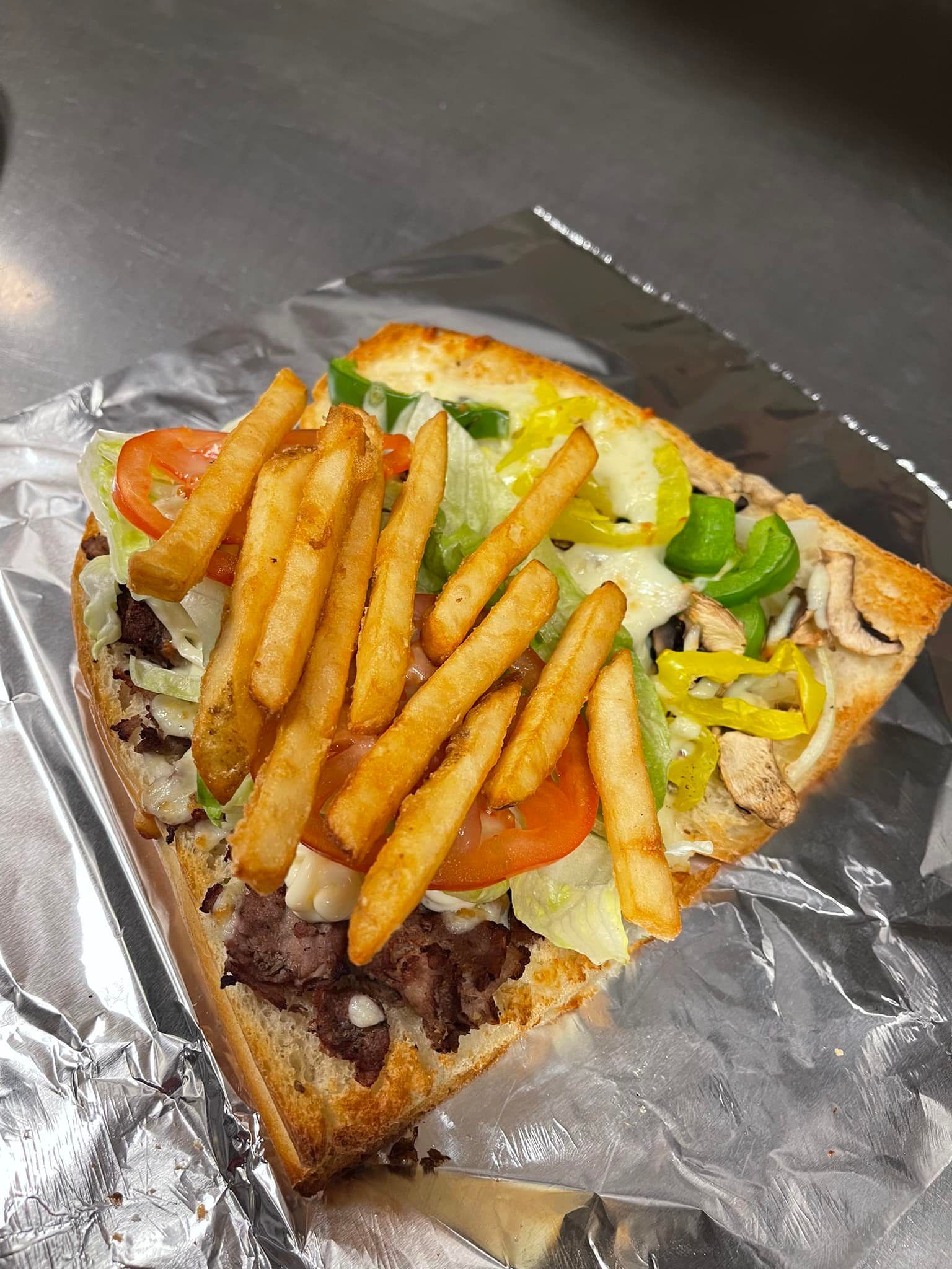 A sub sandwich with french fries on top is wrapped in tin foil.